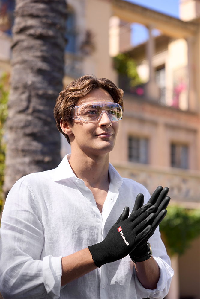 George Russell wears safety glasses and Einhell gloves while standing in the sun in front of a villa.