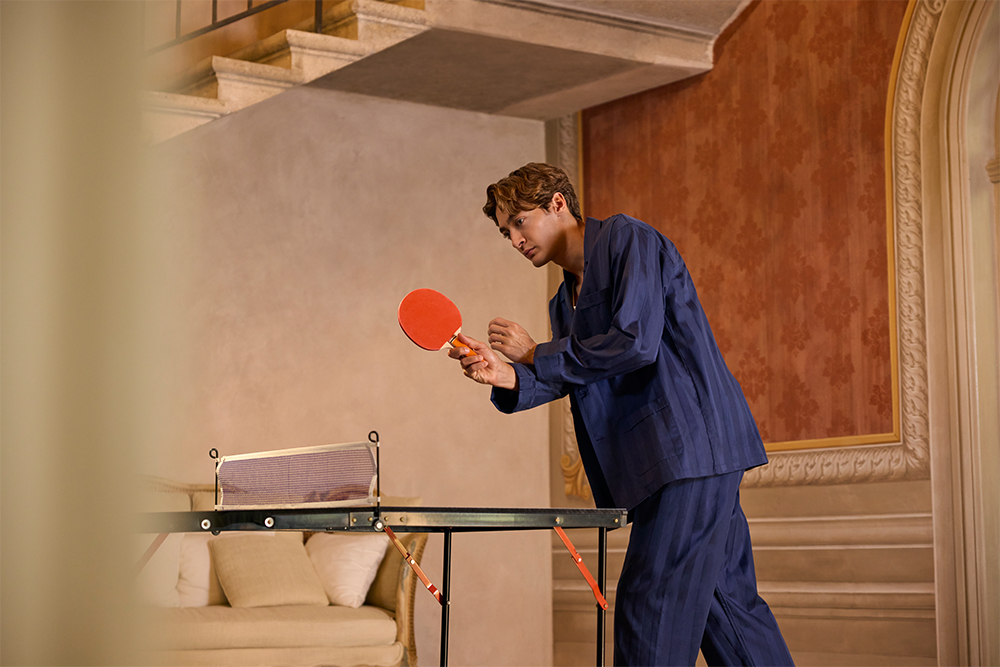 George Russell plays table tennis in a room with red wallpaper and classic interior design.