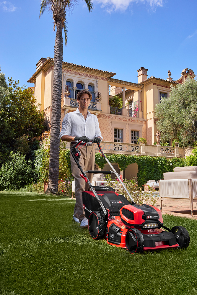 George Russell mows the lawn with an Einhell cordless lawn mower in front of a mediterranean villa.