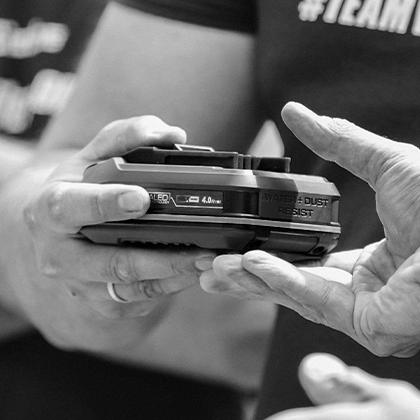 Two people jointly hold an Einhell SEALED battery Power X-Change 4.0 Ah, black and white.