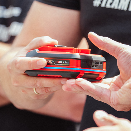 Two people hand over an Einhell SEALED battery Power X-Change 4.0 Ah, shown in color.