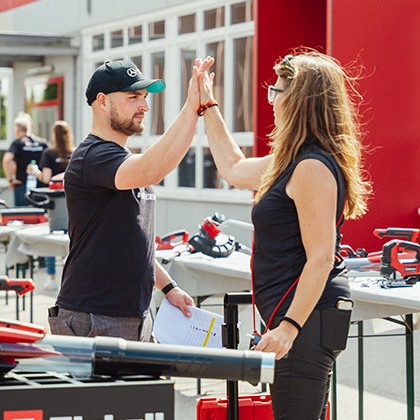 A man and a woman give each other a high five at an outdoor Einhell event with tool displays.
