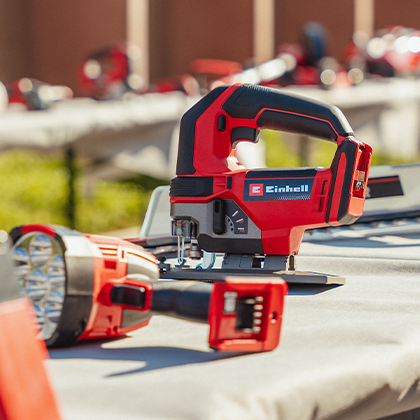 Einhell cordless jigsaw with inserted battery on a table, with an LED cordless lamp in front, in color.